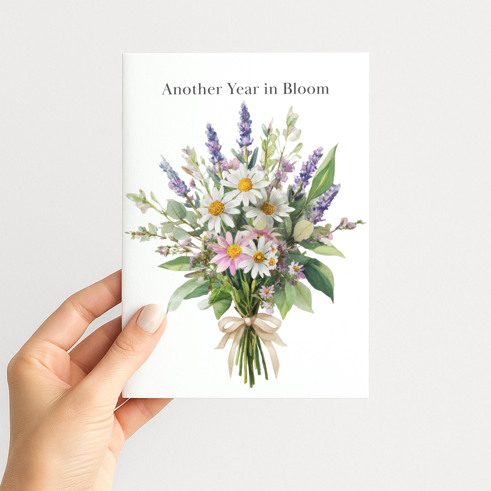 Hand holding Another Year in Bloom birthday card featuring a watercolor wildflower bouquet tied with a ribbon.
