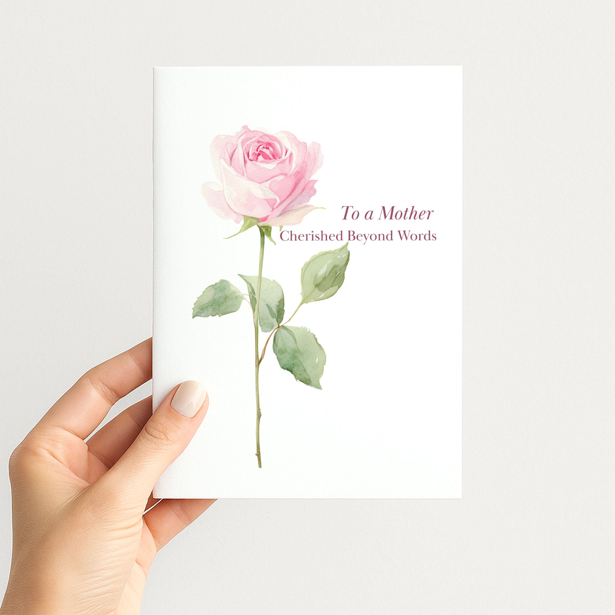 Hand holding a birthday card for Mother featuring a delicate pink watercolor rose and burgundy lettering.