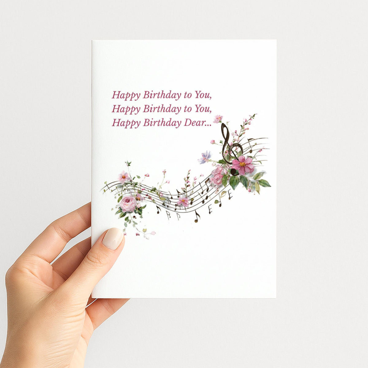Hand holding a birthday card featuring flowing musical notes, a treble clef, and delicate pink flowers.