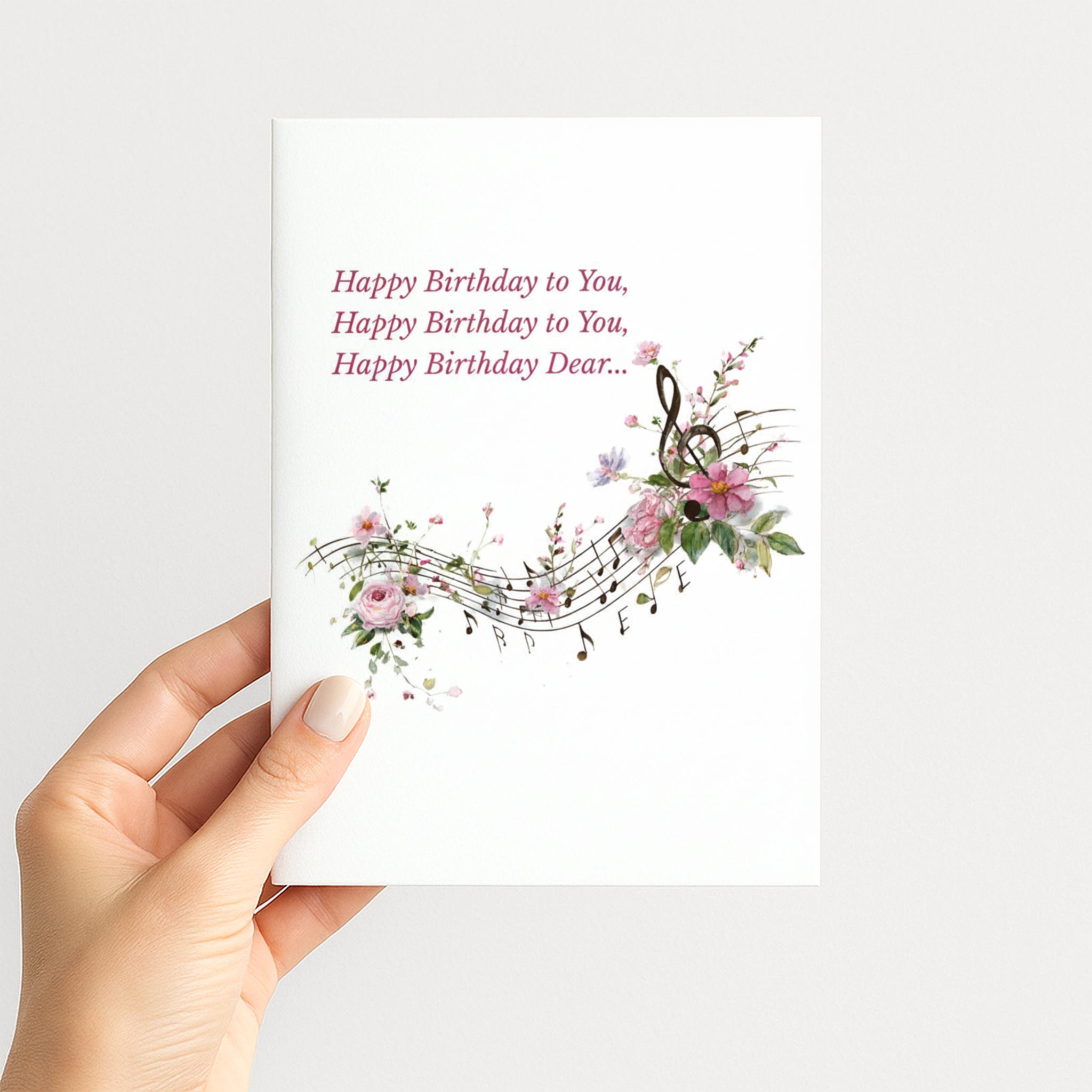 Hand holding a birthday card featuring flowing musical notes, a treble clef, and delicate pink flowers.