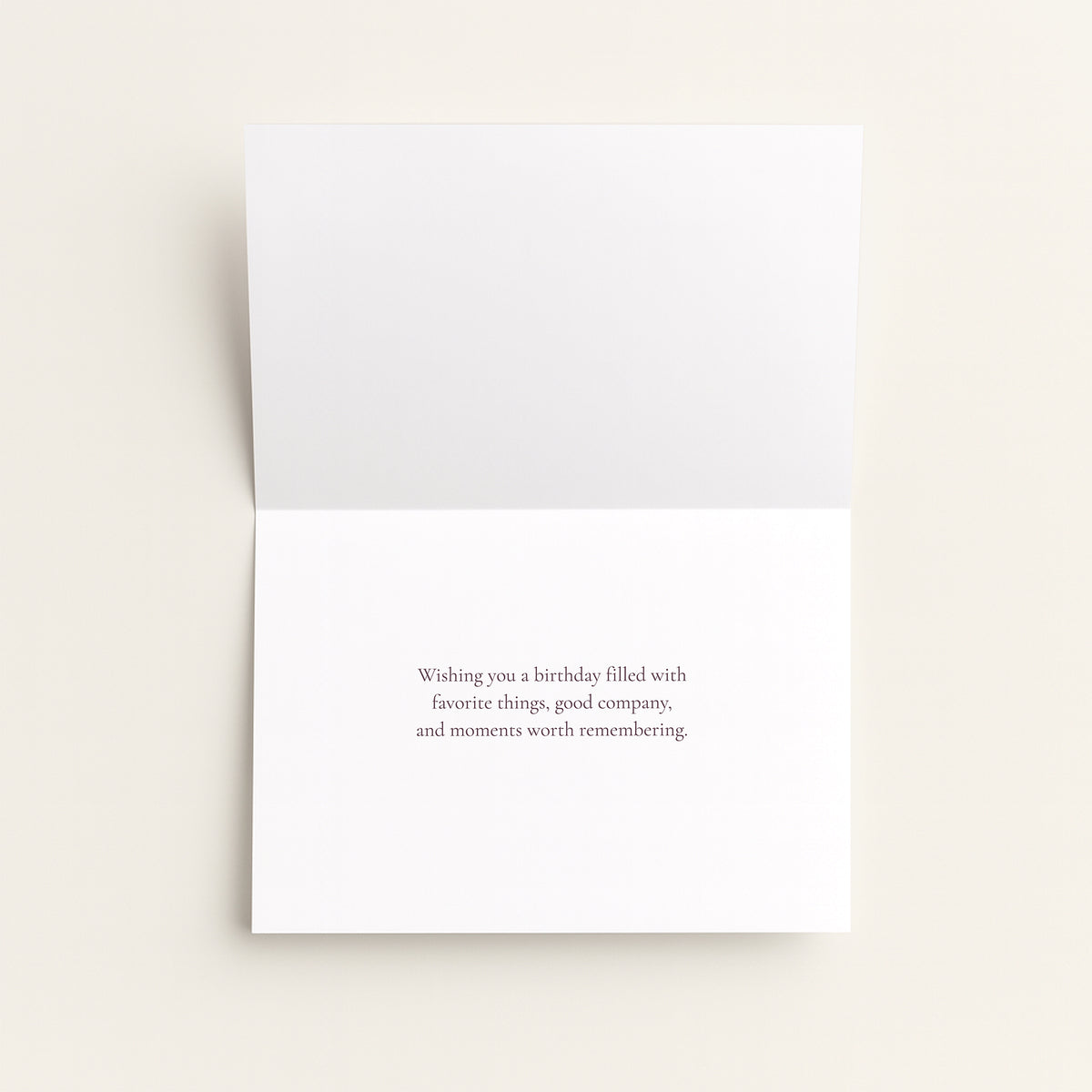 A folded white greeting card with a small centered printed message on the front, photographed on a light warm neutral background.