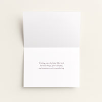 A folded white greeting card with a small centered printed message on the front, photographed on a light warm neutral background.