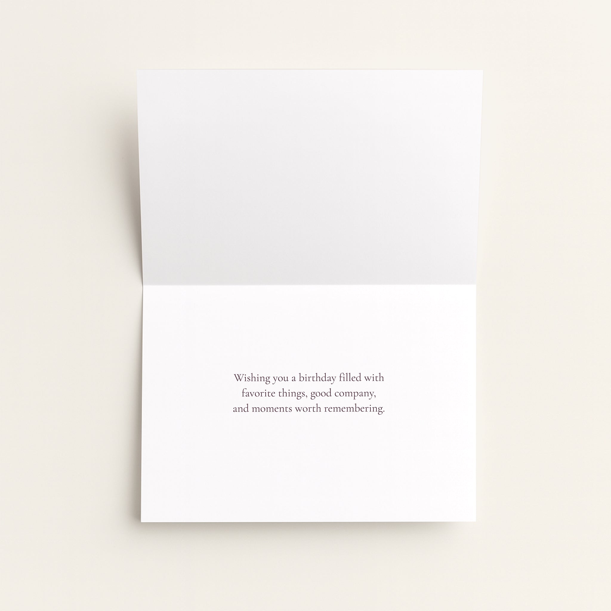A folded white greeting card with a small centered printed message on the front, photographed on a light warm neutral background.