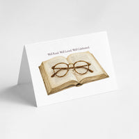 A white A-frame card or sign featuring an illustration of an open book with round eyeglasses on top and the text 'Well Read. Well Loved.
