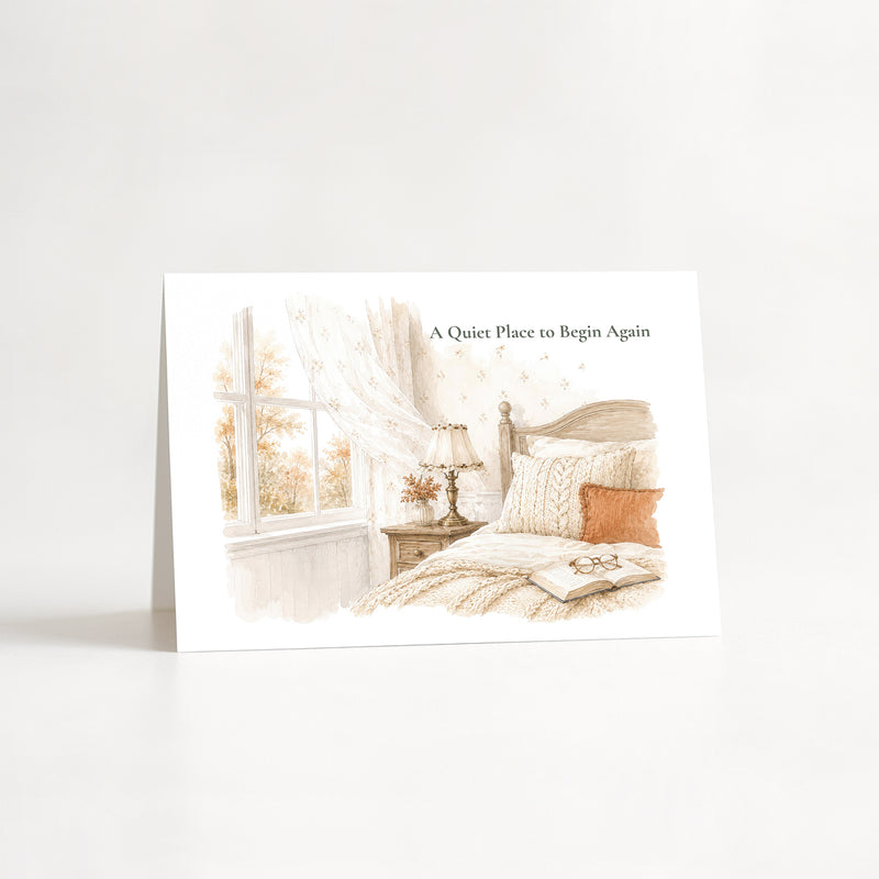 A folded greeting card standing upright on a white surface, featuring a soft watercolor illustration of a cozy bedroom scene with a window, lamp, bed, and the text 'A Quiet Place to Begin Again'.