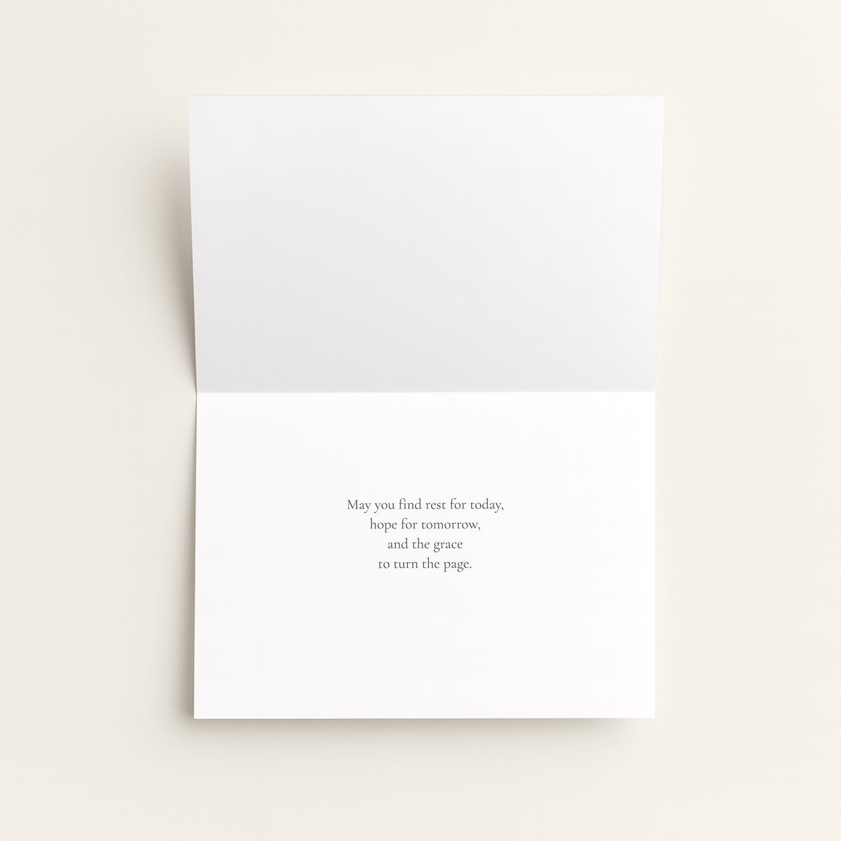A folded white greeting card shown open against a warm off-white background, with a short printed message centered on the lower panel.