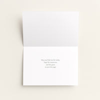A folded white greeting card shown open against a warm off-white background, with a short printed message centered on the lower panel.