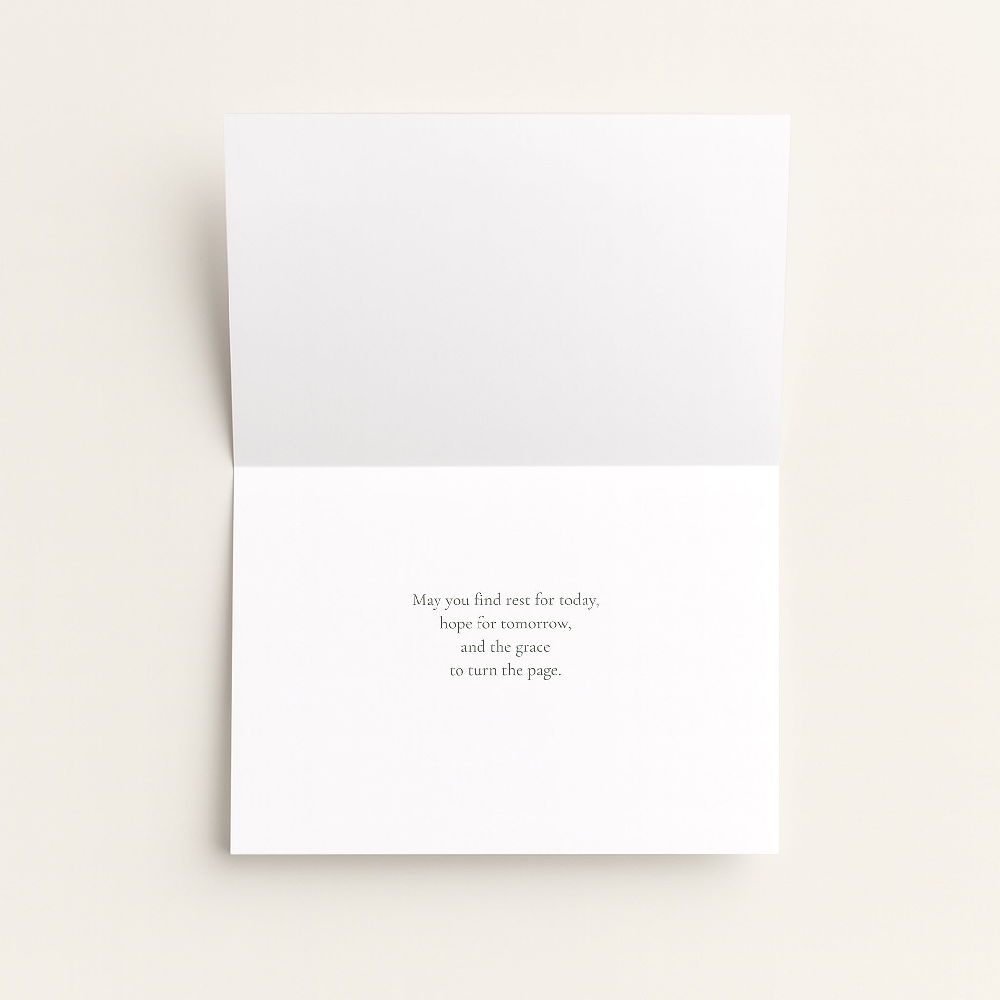 A folded white greeting card shown open against a warm off-white background, with a short printed message centered on the lower panel.