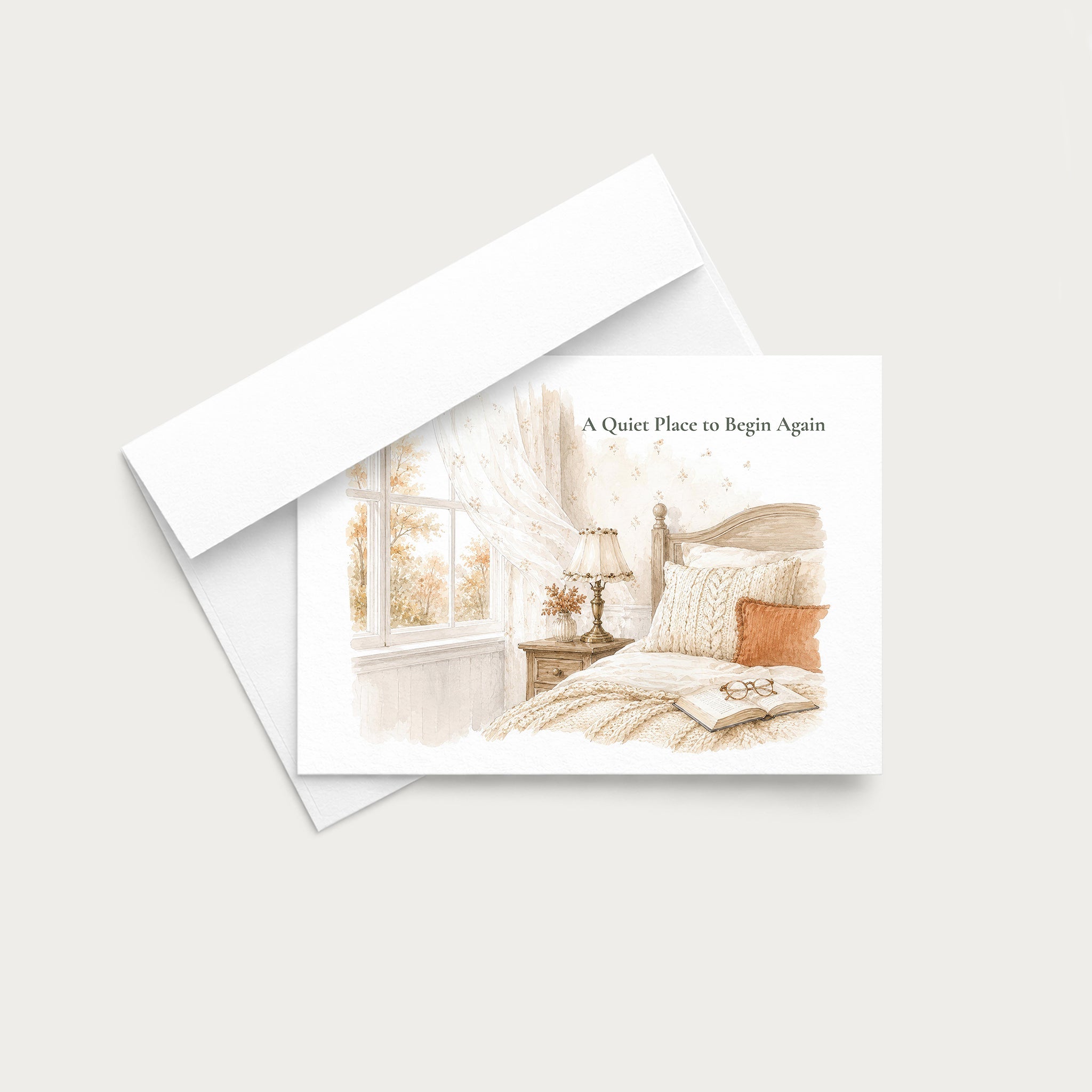 A square greeting card with a watercolor-style illustration of a cozy bedroom scene in soft beige, cream, and light brown tones, with a small orange pillow accent. The card is shown overlapping a white envelope on a light warm gray background.