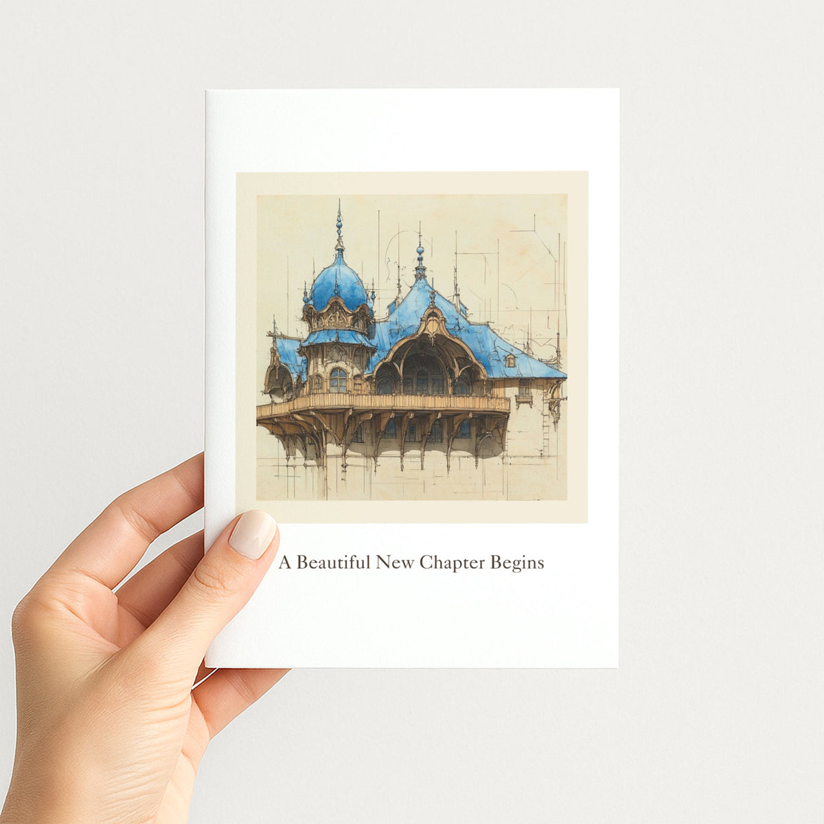 Hand holding a new-home greeting card featuring an elegant blue-roofed architectural illustration.