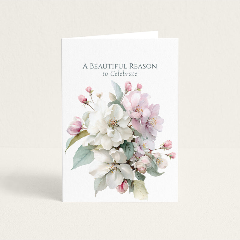 A Beautiful Reason to Celebrate congratulations card with soft pink and white blossoms on textured white paper.