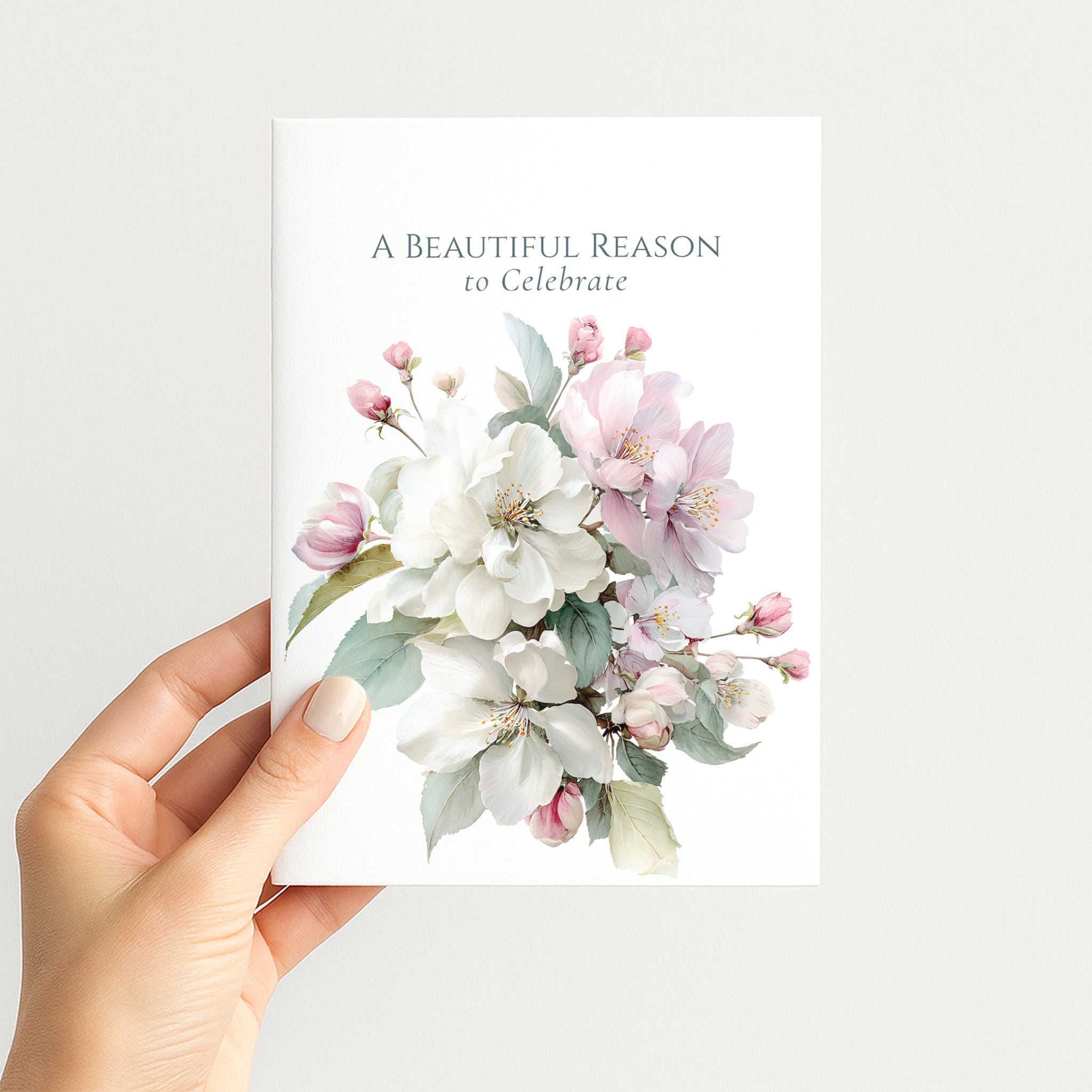 Hand holding A Beautiful Reason to Celebrate card featuring pink and white botanical artwork.