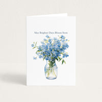 Get-well card featuring a watercolor bouquet of blue forget-me-nots in a glass vase with the message “May Brighter Days Bloom Soon.”