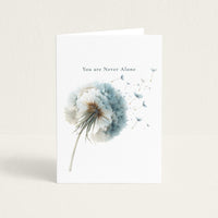 Encouragement card featuring a soft blue watercolor dandelion with seeds drifting away beneath the words “You are Never Alone.”
