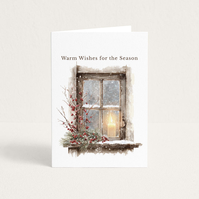 Seasonal greeting card featuring a snowy rustic window, glowing candle, evergreen branches, and red berries beneath the words “Warm Wishes for the Season.”
