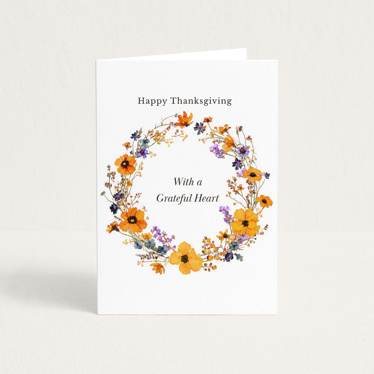 Thanksgiving greeting card featuring a delicate autumn floral wreath in orange, purple, and blue with “With a Grateful Heart.”