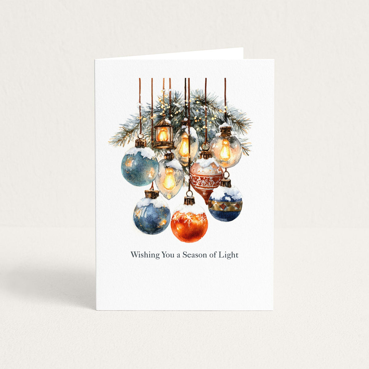 Wishing You a Season of Light holiday card featuring watercolor ornaments, glowing lanterns, and snowy evergreen branches.