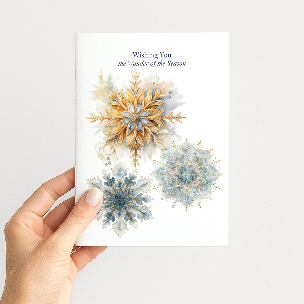 Hand holding a holiday card decorated with elegant blue and gold snowflakes and “Wishing You the Wonder of the Season.”