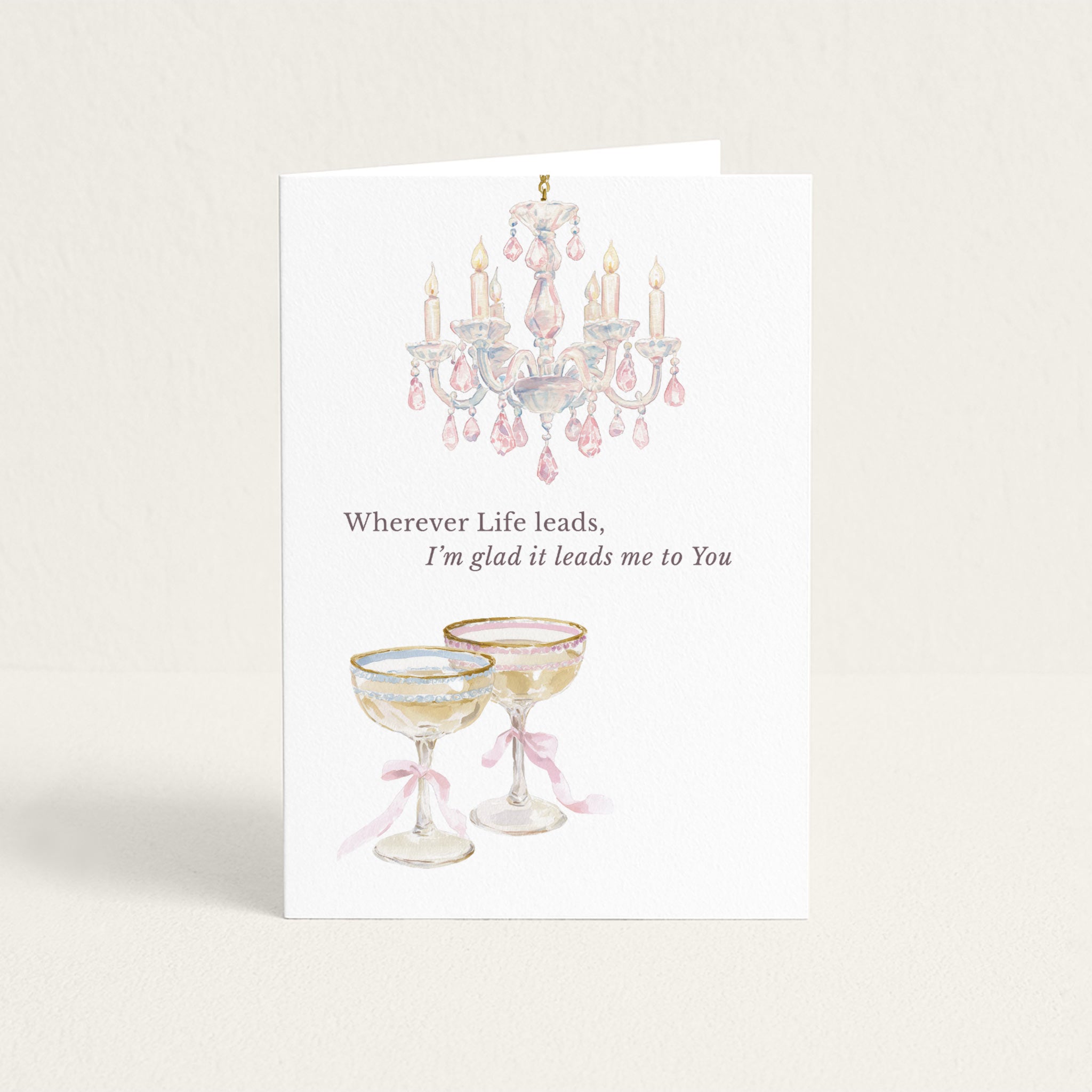 Romantic greeting card featuring a watercolor pink crystal chandelier and two ribbon-tied champagne coupes with the message “Wherever Life leads, I’m glad it leads me to You.”