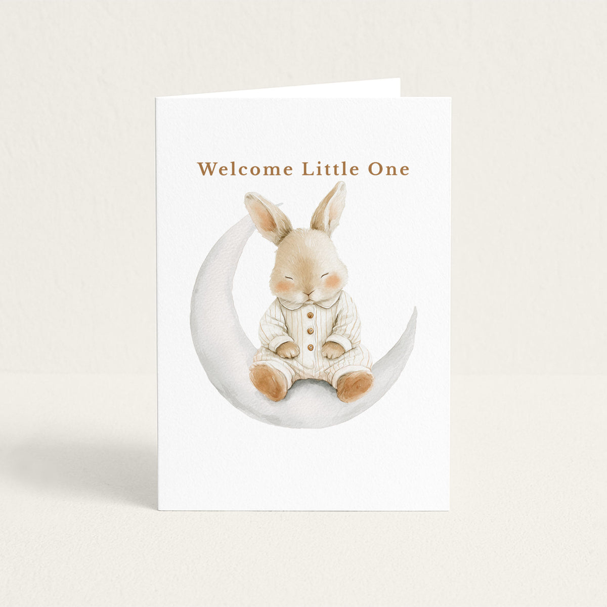New baby greeting card featuring a watercolor bunny in striped pajamas seated on a crescent moon beneath the words “Welcome Little One.”