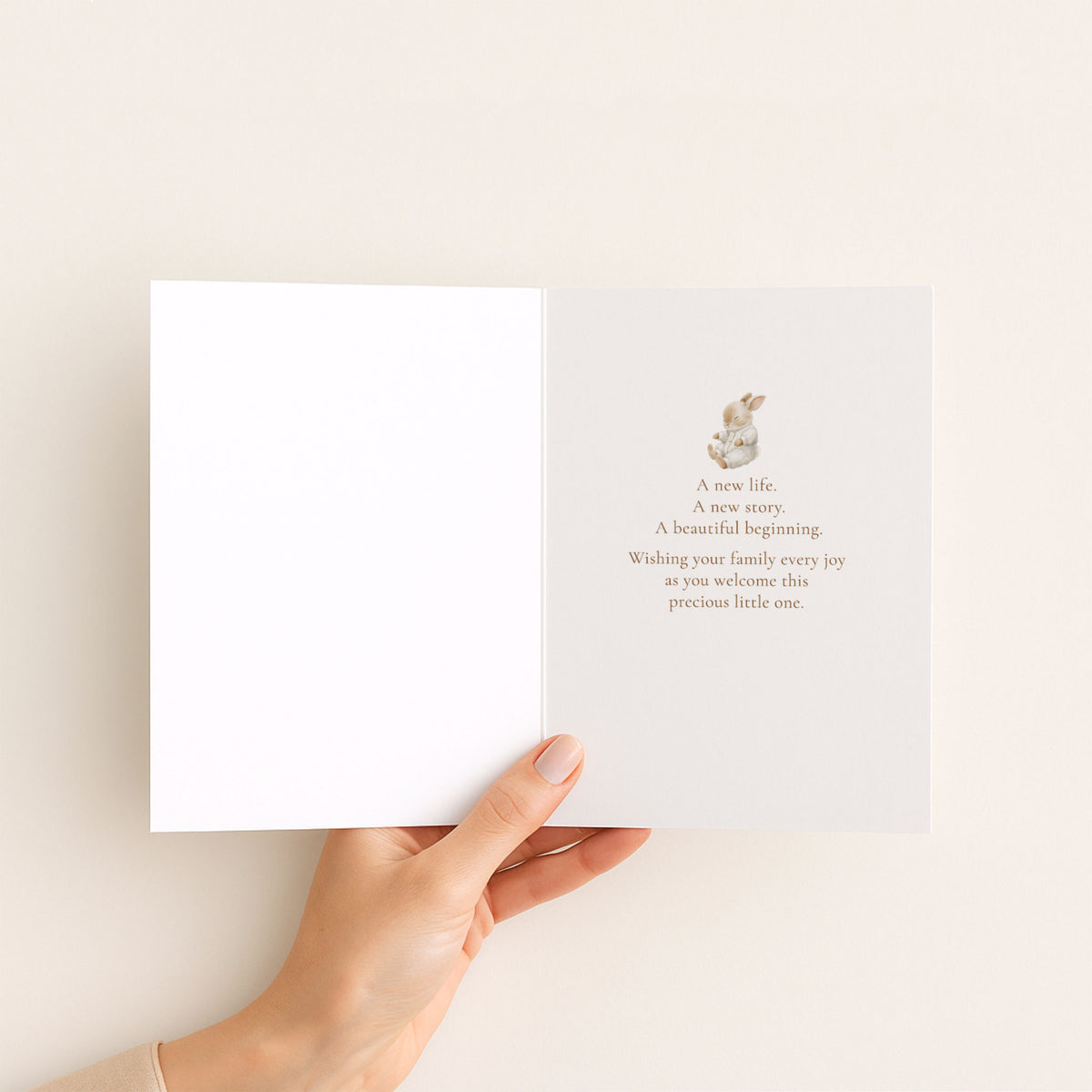 Open new baby card held in hand, showing a small bunny illustration and a message celebrating a new life, new story, and beautiful beginning.