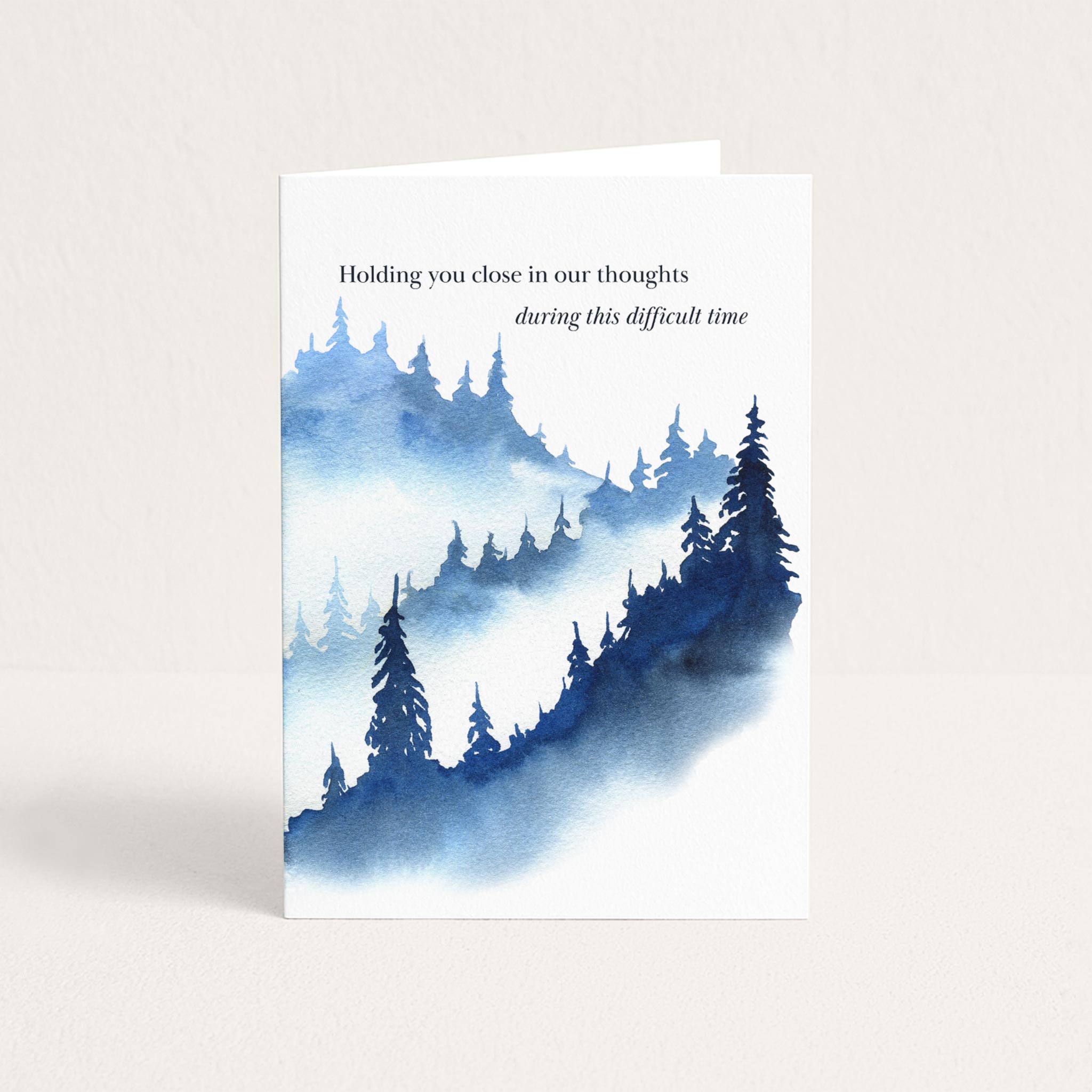Blue watercolor forest sympathy card with the message “Holding you close in our thoughts during this difficult time.”