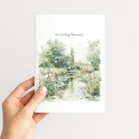 Hand holding a sympathy greeting card illustrated with a peaceful watercolor garden pond and wildflowers.