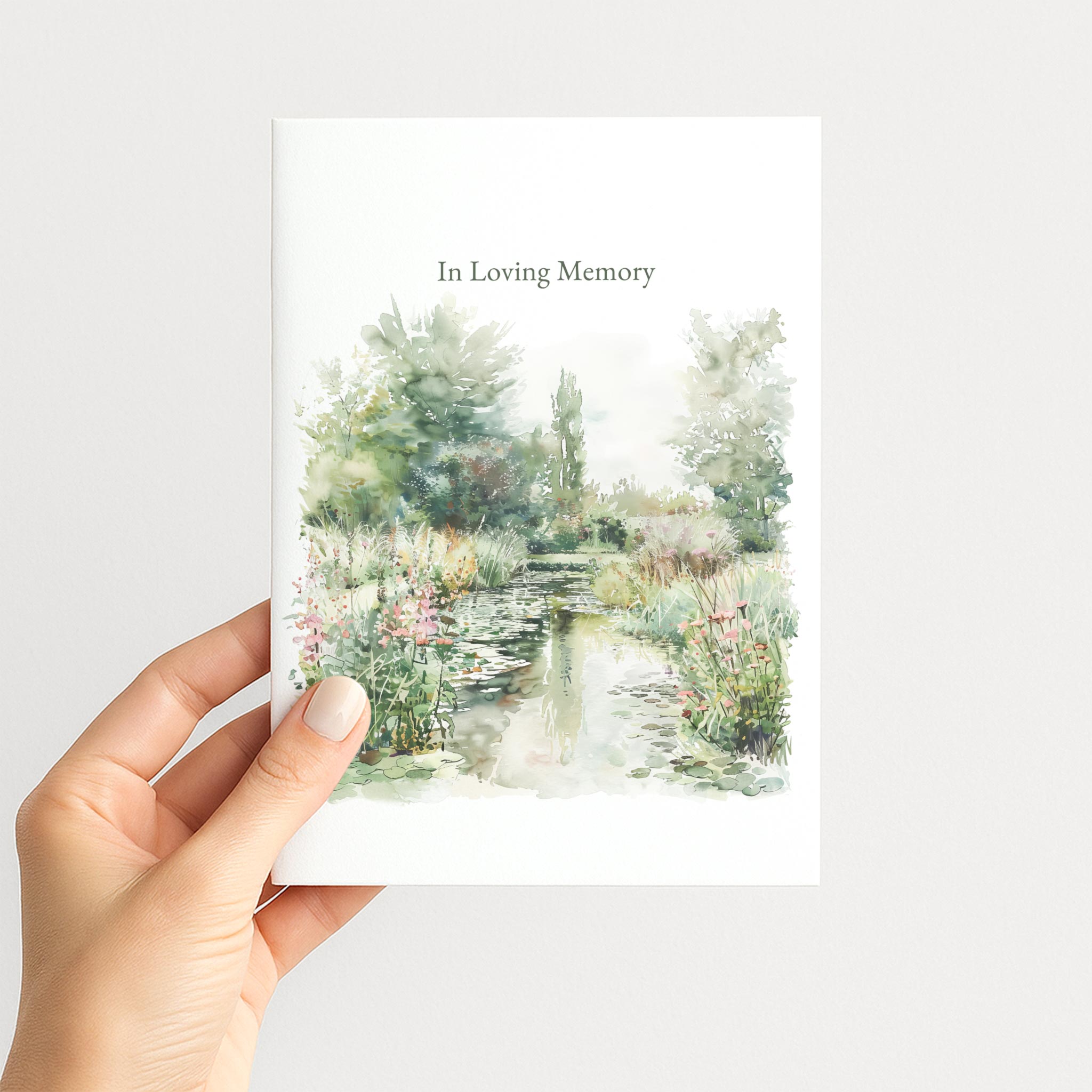 Hand holding a sympathy greeting card illustrated with a peaceful watercolor garden pond and wildflowers.
