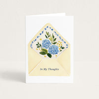 Thinking-of-you greeting card featuring a pale yellow envelope filled with blue hydrangeas and small yellow flowers, with the words “In My Thoughts.”