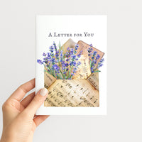 Hand holding A Letter for You card featuring lavender, vintage correspondence, and musical notation.