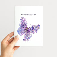 Hand holding a bride-to-be card featuring a purple butterfly with lilac floral details.
