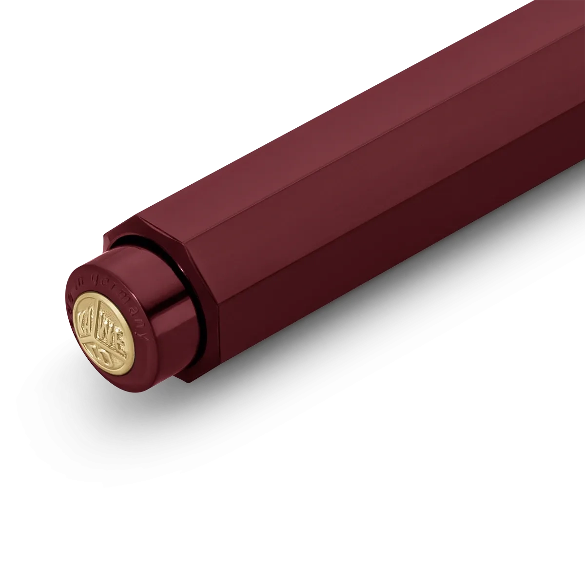 A close-up of a metallic burgundy cylindrical product, showing a hexagonal body and a circular gold-toned cap with embossed branding, set against a plain white background.