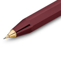 A close-up of a faceted metallic pen tip in deep burgundy with a polished gold conical accent and fine gray tip, shown on a clean white background.
