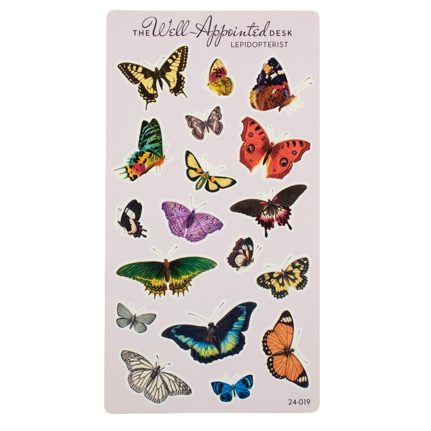 A sheet of butterfly-shaped desk stickers on a pale pink card, with the text 'The Well Appointed Desk' and 'Lepidopterist' at the top. The sheet contains multiple colorful illustrated butterflies in yellow, orange, green, purple, blue, black, and white.