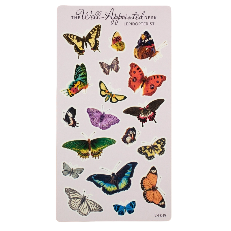 A sheet of butterfly-shaped desk stickers on a pale pink card, with the text 'The Well Appointed Desk' and 'Lepidopterist' at the top. The sheet contains multiple colorful illustrated butterflies in yellow, orange, green, purple, blue, black, and white.