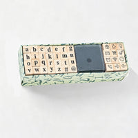 A miniature keyboard-shaped gift box with wooden alphabet and symbol blocks, a black square center piece, and a green patterned outer box, photographed on a white background.