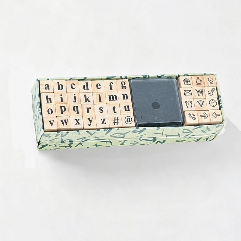 A miniature keyboard-shaped gift box with wooden alphabet and symbol blocks, a black square center piece, and a green patterned outer box, photographed on a white background.