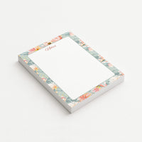 Blush Garden memo pad shown at an angle with a watercolor border of coral, blush, and ivory flowers on a misty sage background.