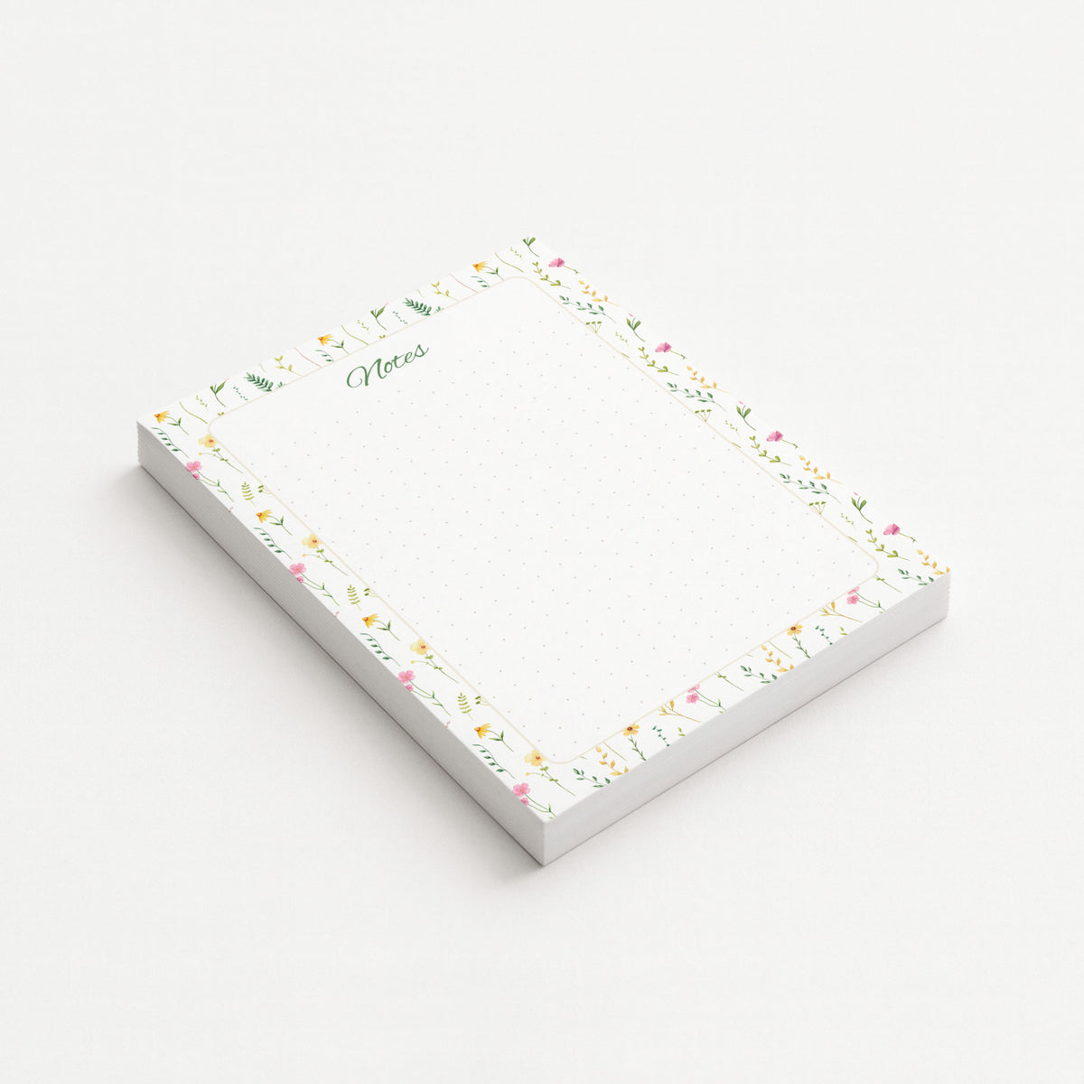 Wildflower Meadow memo pad shown at an angle with delicate pink and yellow wildflowers, green botanical sprigs, and a subtly dotted writing area.