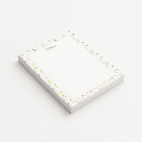 Wildflower Meadow memo pad shown at an angle with delicate pink and yellow wildflowers, green botanical sprigs, and a subtly dotted writing area.