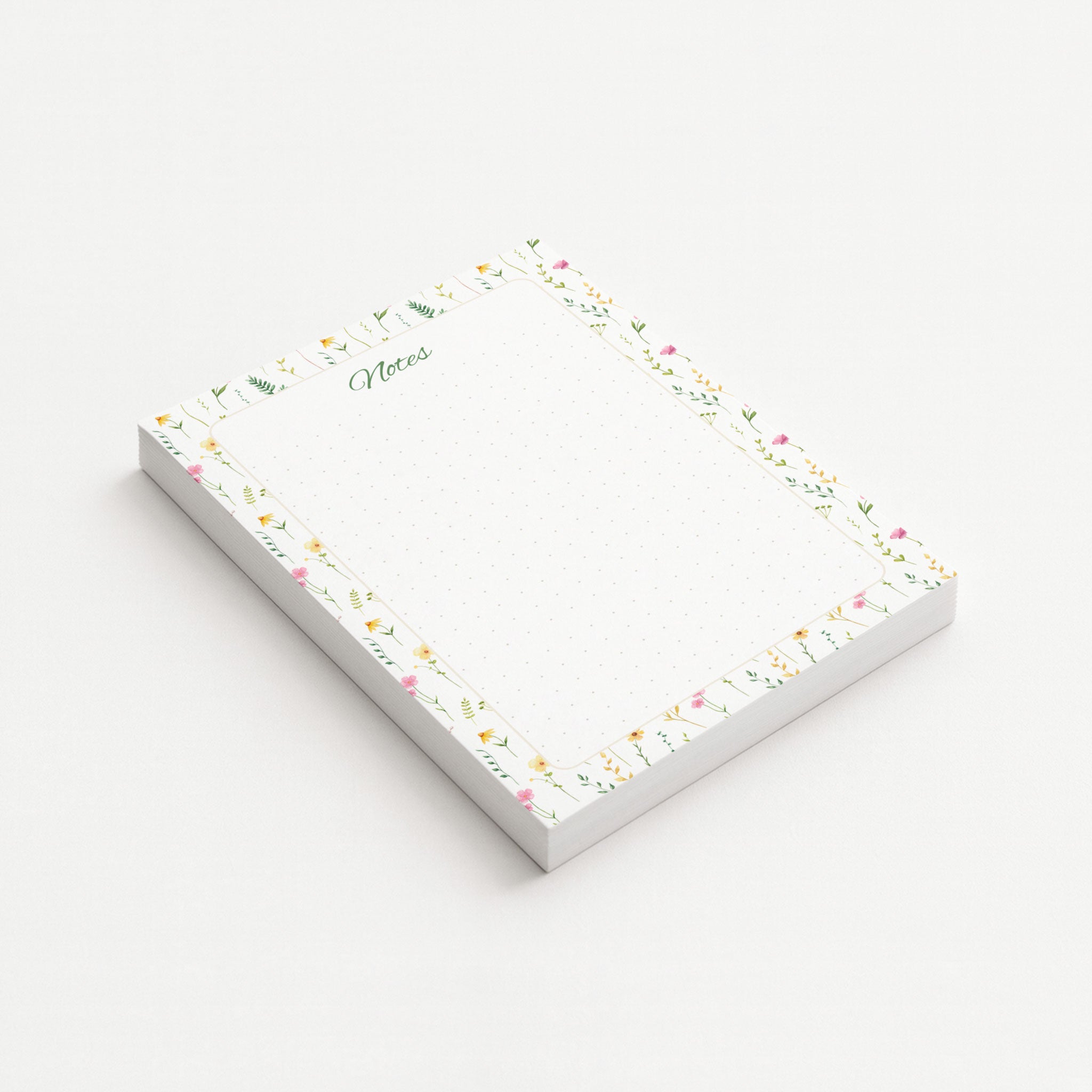 Wildflower Meadow memo pad shown at an angle with delicate pink and yellow wildflowers, green botanical sprigs, and a subtly dotted writing area.