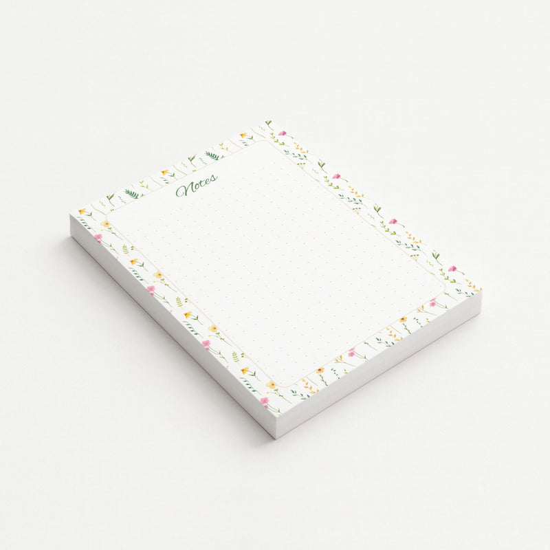 Wildflower Meadow memo pad shown at an angle with delicate pink and yellow wildflowers, green botanical sprigs, and a subtly dotted writing area.
