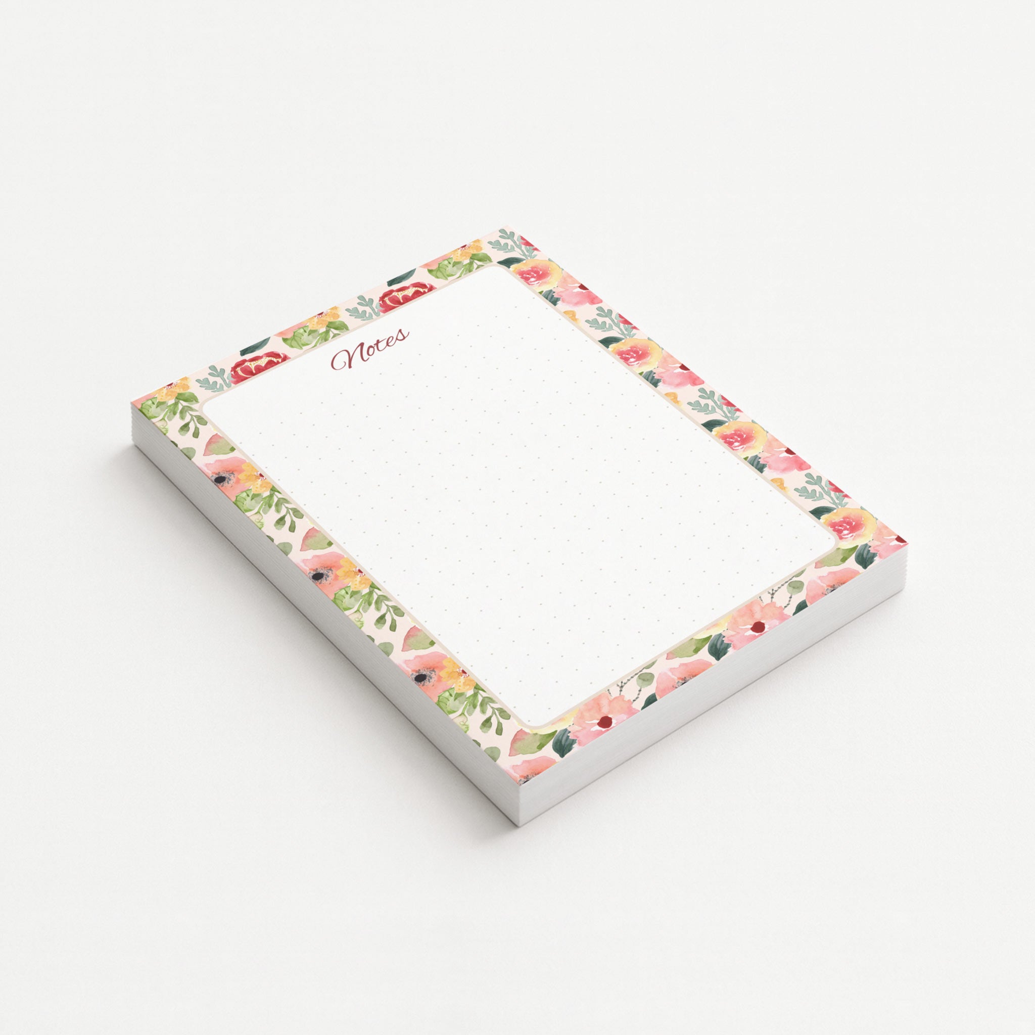 Painter’s Garden memo pad shown at an angle with a watercolor border of blush, coral, yellow, and red flowers surrounding a subtly dotted writing area.