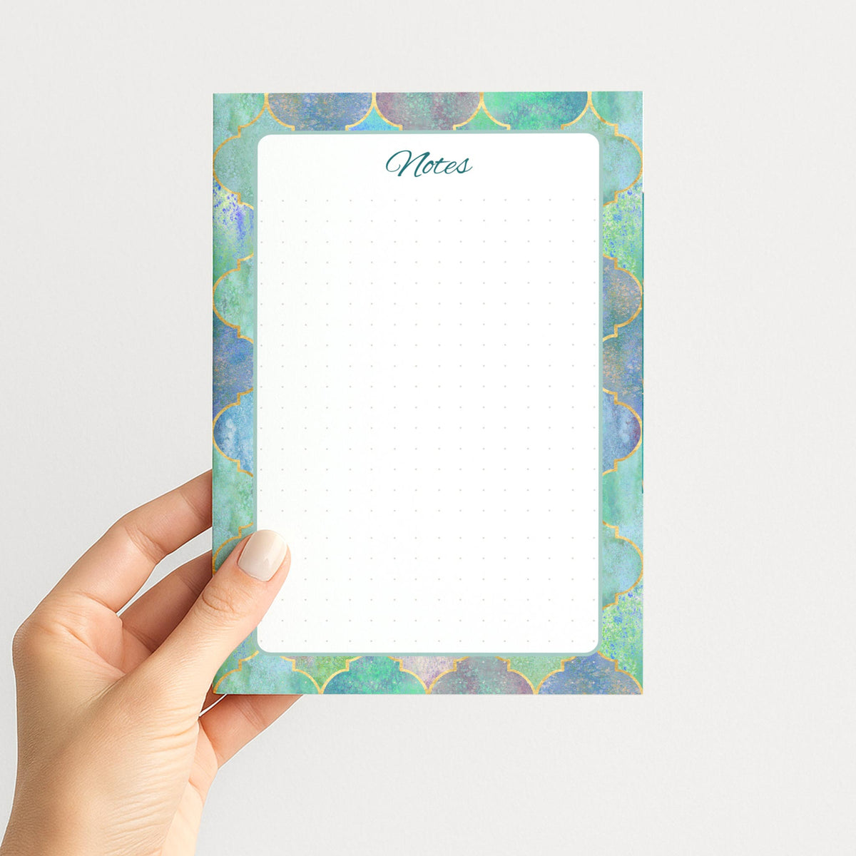 Hand holding the Gilded Mosaic memo pad upright, showing its teal Notes heading, rounded writing panel, and colorful gold-detailed border.
