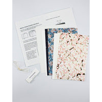 Open pamphlet-stitch bookbinding kit with printed instructions, floral Chiyogami cover papers, interior pages, bookbinding needle, and thread.