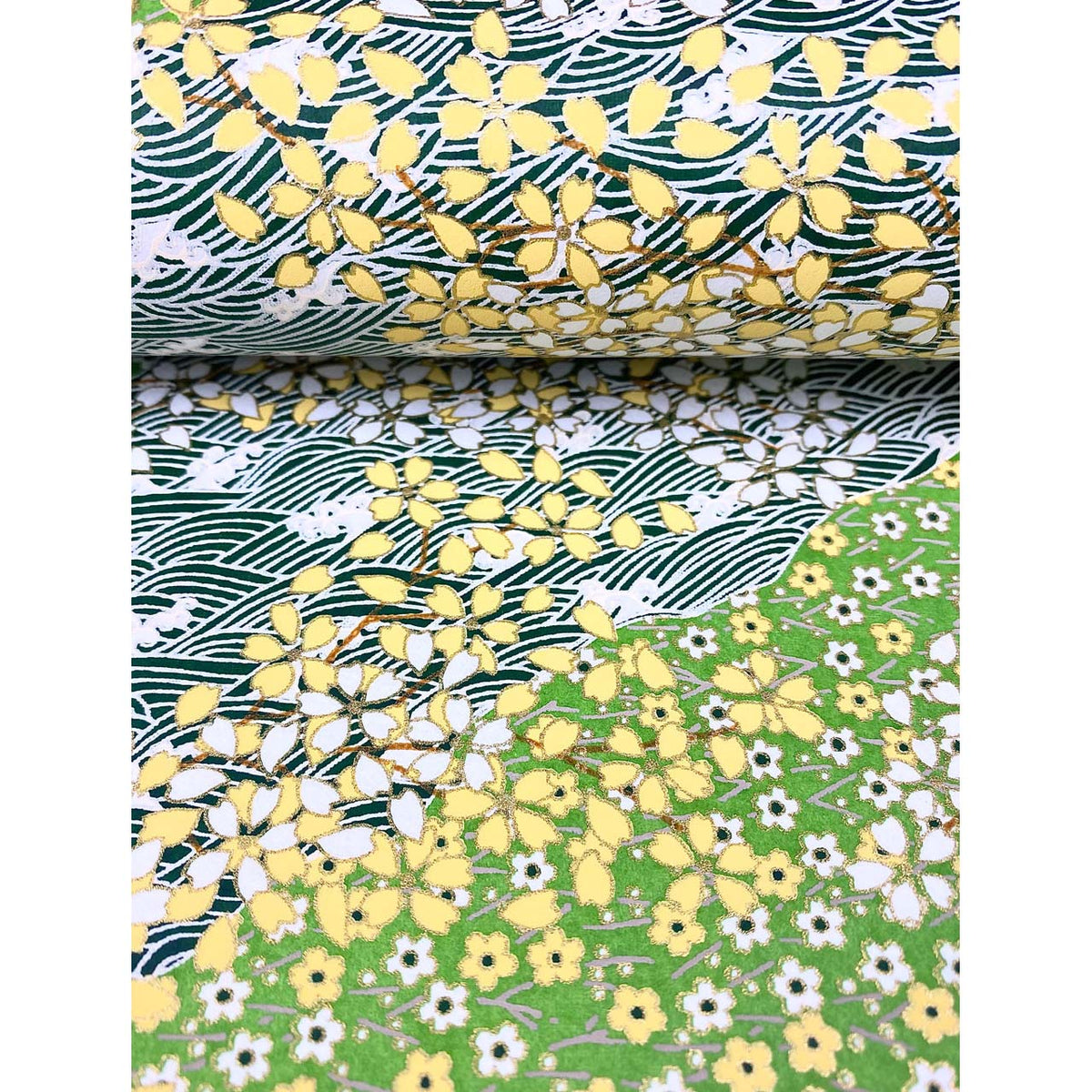 Close-up of hand silk-screen printed Chiyogami paper showing green garden bands, delicate blossoms, leafy branches, and dark wave patterns. This paper is bent like the page of a book.