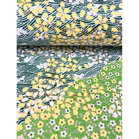 Close-up of hand silk-screen printed Chiyogami paper showing green garden bands, delicate blossoms, leafy branches, and dark wave patterns. This paper is bent like the page of a book.