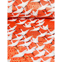 Close-up of hand silk-screen printed Chiyogami paper showing white cranes, black details, and warm gold wave motifs on red.