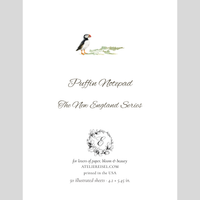 A product presentation of a Puffin Notepad from Ateリエisei, featuring a watercolor puffin illustration on a white page surrounded by a gray border. The text details the 'The New England Series' and includes a monogram logo.