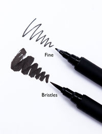 Close-up of a Sakura bristle brush pen showing its flexible brush tip and jet-black pigment ink strokes.
